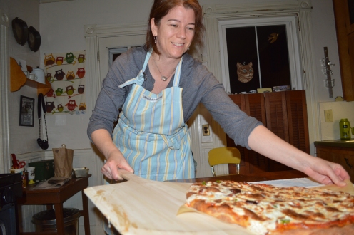 Jen pulls a steaming hot pizza pie out of the oven.